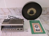 General view of clock radio, C. Crane Co. Select-A-Tenna and paperwork, all arranged on a white surface