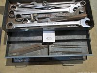 Top view of open top drawer showing combination wrenches and various files arranged inside compartments.