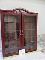 Front closed view showing red-stained wood, arched top with carved detail, two etched glass doors with metal handles.