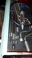 Photo showing main air tool with air hose connector and several metal attachment rods and bent extensions laid out on a dark surface.