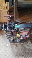 Black metal Basil bike basket filled with coiled locking cable and visible red Norco hand pump handle behind basket