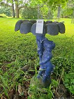 Front and side views of blue stone cherub fountain statue on grass and surrounded by small rocks, showing flower-shaped basin and cherub figure.