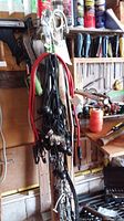 Photo of hanging chains with attached hooks and red elastic cover ties with hooks, mounted on a wooden board with various tools in background.