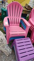 Front view of stack of pink and blue plastic Adirondack chairs with purple stools in front