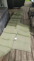 Four green patio chair cushions arranged on a wooden deck, showing tufted stitching and moderate padding.