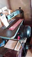 Full side view showing the Delta scroll saw mounted on a work surface including the blade area, arm, and electric motor below.