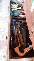 Tools including files, chisels, hand saw, and planer inside an open wooden drawer