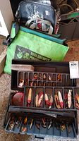 Top view of multiple fishing lures and weights organized in plastic trays with a carry bag behind them.