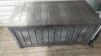 Full front view of a rectangular plastic storage box with wood panel texture, showing length and faded brown color.
