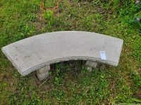 Full top view showing the curved stone or concrete bench with decorative edges and weathered surface on grass.