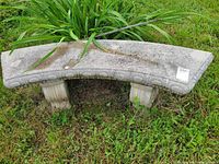 Photo of curved stone or concrete garden bench on grass, showing carved circular pattern and signs of wear