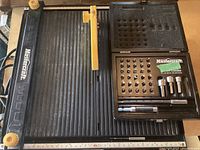Top view of the Mastercraft table saw with yellow safety guard and the Mastercraft drill bit set in its open case on the saw's surface.