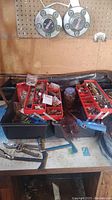 Black plastic tool box filled with three red organizers containing mixed hardware and small tools.