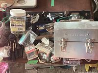 Photo showing overall collection of tools, fasteners in containers, hand tools, and metal lunch box on top of a green case.