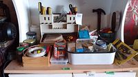 Overview of tools and hardware on surface including white organizer, hammer, jars, tapes, and metal container.