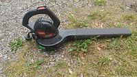 Full side view of the black Toro Power Sweep leaf blower lying on grass and gravel, showing the entire blower and nozzle tube