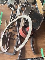Rusted metal box holding a red metal can and other items, with ice/hay tongs and other tools on a wooden surface.