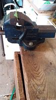 Blue cast metal bench vise fixed to wooden workbench, showing full vise profile and handle.