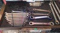 Photo showing a set of combination wrenches, some ratcheting spanners, and other open/box-end wrenches arranged on a black surface.