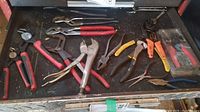 Overview of assorted hand tools in a drawer showing various pliers, wrenches, wire strippers and grips mainly with red handles.