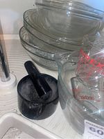 Stacked clear Pyrex glass mixing bowls and casserole dishes with red-marked Pyrex measuring cups and small black mortar and pestle on a drying rack
