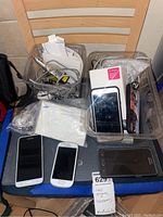 Photo of Samsung smartphones and cell phone accessories in clear bins on a chair, showing multiple phones and accessories untested.