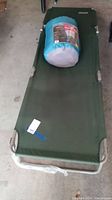 Green metal framed Coleman folding cot with sleeping bag placed on top.