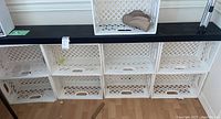 Nine white plastic lattice-pattern storage crates stacked in three rows, three crates per row with a black floating shelf on top.