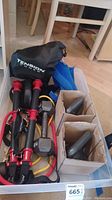 Photo showing Tension Toner branded carrying bag and resistance bands with foam handles and metal clips, two cardboard boxes with weights inside, blue leg weights, yellow resistance bands visible inside plastic storage bin.