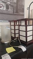Photo showing two Asian style square table lamps with wooden frames and cream panels, and one crackled glass lamp with frosted cylindrical shade on metal base.