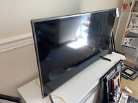Side angle showing the thin profile and silver bezel/frame of the LG 48-inch TV on a white cabinet
