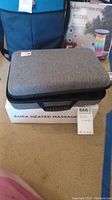 Gray padded carrying case on top of Aura Heated Massage box with tag
