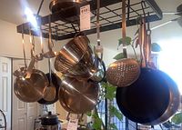 Photo showing multiple stainless steel pots and pans hanging on a black metal pot rack with various cooking utensils.