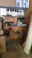 Photo showing metal wire shelving unit filled with various items including boxes and bags in an unfinished storage space.