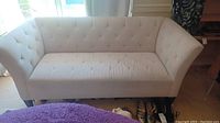 Full front view of cream colored tufted sofa with visible wrinkling on seat cushions and wooden legs.