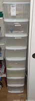 Photo showing eight clear plastic stackable storage containers with white lids, stacked vertically.