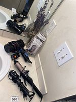 View of the blow dryer, curling iron, and straightener on a bathroom counter near a sink and mirror.