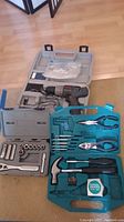Photo showing Ryobi cordless drill in gray case along with a Craftsman socket set and a blue hand tool set case containing pliers, hammer, screwdrivers, tape measure, and utility knife.