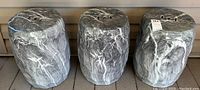 Three gray ceramic garden stools with white marbling placed side by side on a deck, showing full height and shape.