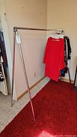 FoldRak clothing rack viewed from the front with a red dress and other clothes hung on plastic hangers.