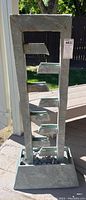 Front view of entire water feature fountain showing vertical tiered channels and base with stones
