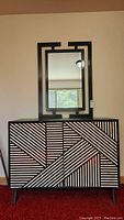 Front view of dresser and wall mirror showing black and white geometric inlay design on dresser doors and mirror frame.