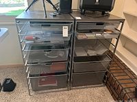 Front view of two metal mesh drawer storage units with items inside drawers and dark wood tops.