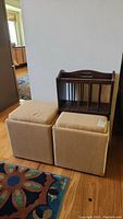 Two beige upholstered storage footstools alongside a dark wood magazine holder with vertical dividers and carrying handle.