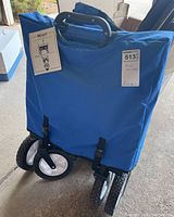 Photo of the folded blue sports wagon showing frame, wheels, and attached tag.