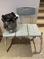 Clear therapy ice machine labeled 'Iceman Clear' on a gray plastic shower bench with backrest and adjustable legs.