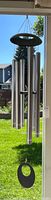 Full view of the large wind chime hanging outdoors showing all metal chimes and the black circular wind catcher at the bottom.