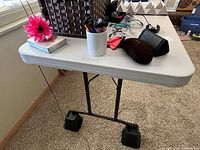 White plastic folding table with some personal items on top, showing corner and surface condition.