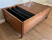Front and side view of wooden mid century modern coffee table showing outer wood grain and black magazine insert compartments.