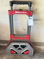 Milwaukee folding hand cart standing upright with handle extended and platform folded up.
